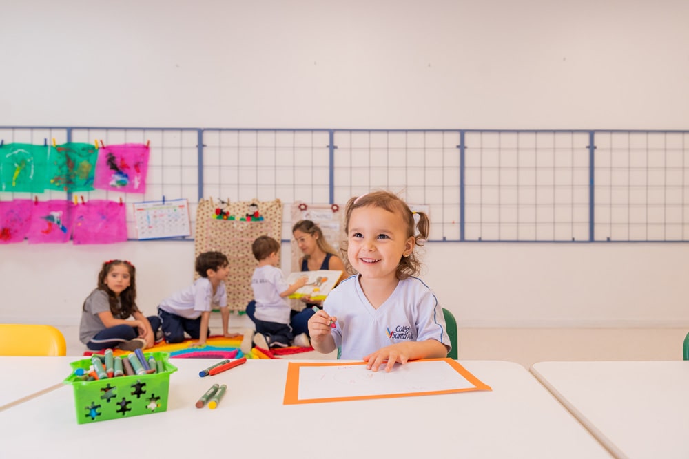 Foto: Garotinha sorrindo enquanto desenha com giz de cera