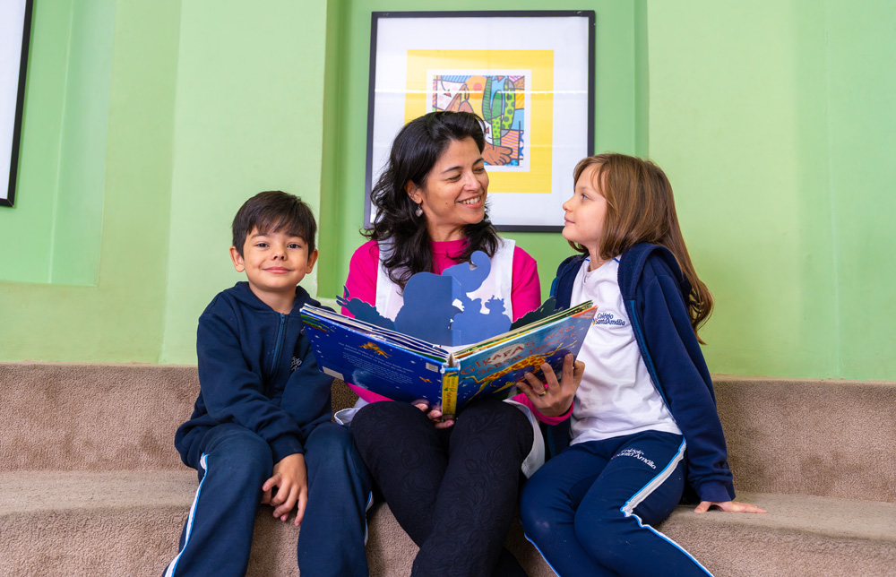 Foto: Professora lendo livro com alunos em ambiente confortável